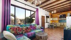 Una sala de estar con un sofá colorido, una mesa de centro de madera y una zona de cocina con armarios y un refrigerador.