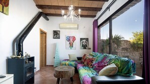 Una sala de estar acogedora con chimenea, un sofá de colores, un taburete de madera y obras de arte en las paredes.
