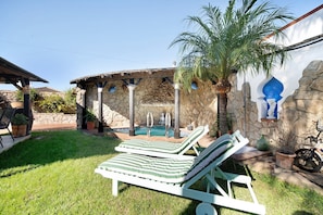 Un patio con dos sillones de descanso, un muro de piedra, una palmera y una pequeña piscina.