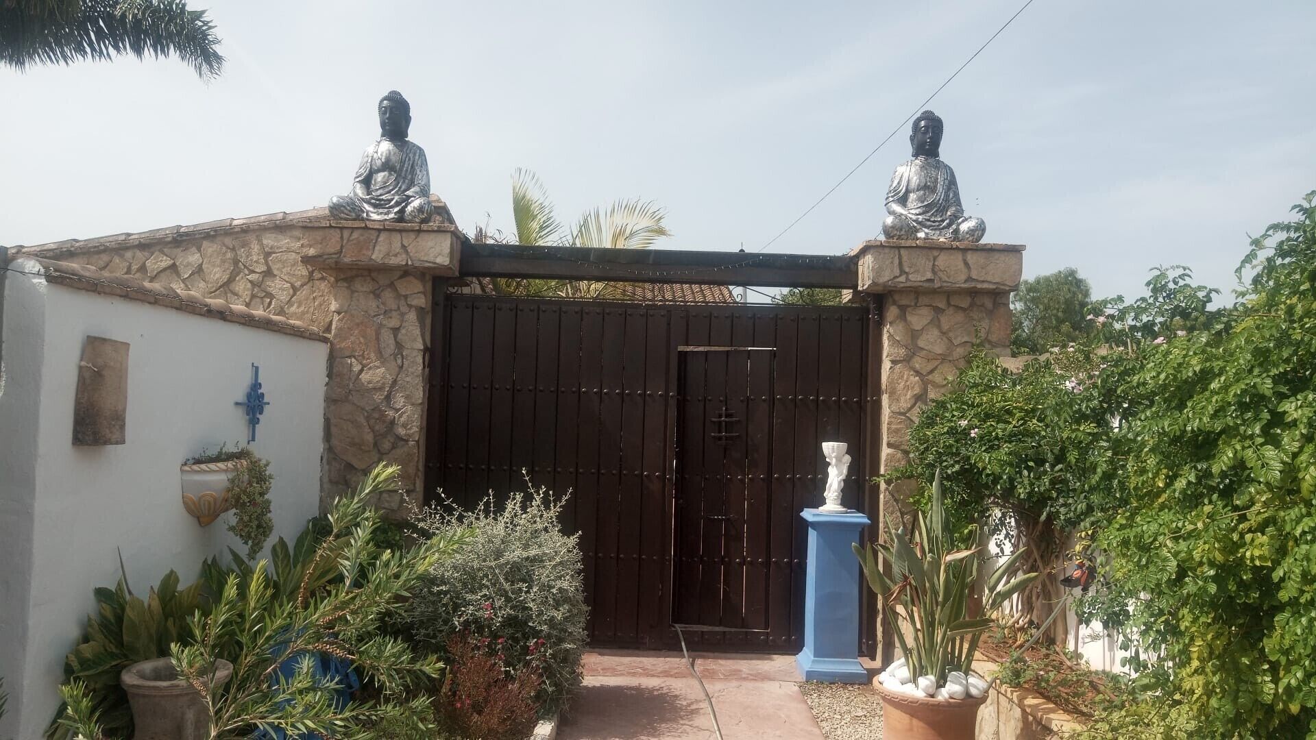 A gated entrance with a stone wall, two statues, and potted plants.