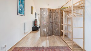 A hallway with a wooden floor, a patterned rug, a wardrobe with decorative panels, and a wooden shelving unit.