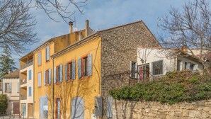 A street view with buildings featuring balconies, a stone wall, and a clear sky.