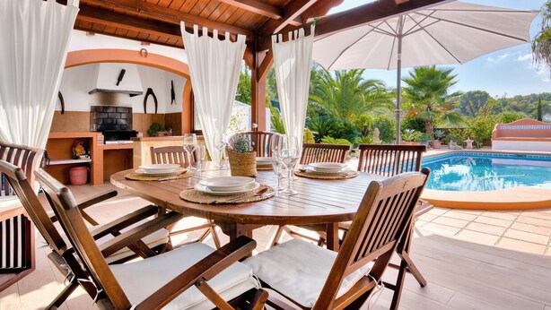 An outdoor dining area with a pool, wooden furniture, and a grill.