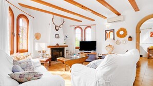 A living room with white furniture, wooden beams, a fireplace, and a television.