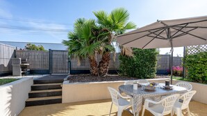 An outdoor patio with a table and chairs, a palm tree, and a fence. - La Tourette – Charming, Unique Cottage with Private Terrace, Garden, and Wi-Fi (Jard Sur Mer)