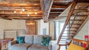 A rustic interior with exposed wooden beams, a sofa with patterned cushions, a wooden chair, and a staircase. - La Tourette – Charming, Unique Cottage with Private Terrace, Garden, and Wi-Fi (Jard Sur Mer)