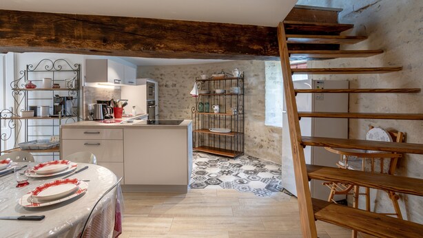 A kitchen with a central island, a dining area with a table set for four, and a staircase leading to an upper level. - La Tourette – Charming, Unique Cottage with Private Terrace, Garden, and Wi-Fi (Jard Sur Mer)