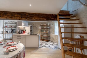 Una cocina con una isla central, un comedor con una mesa preparada para cuatro personas y una escalera que sube a un nivel superior.