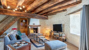 A loft-style living room with exposed wooden beams, a fireplace, a television, and a cozy seating area.
