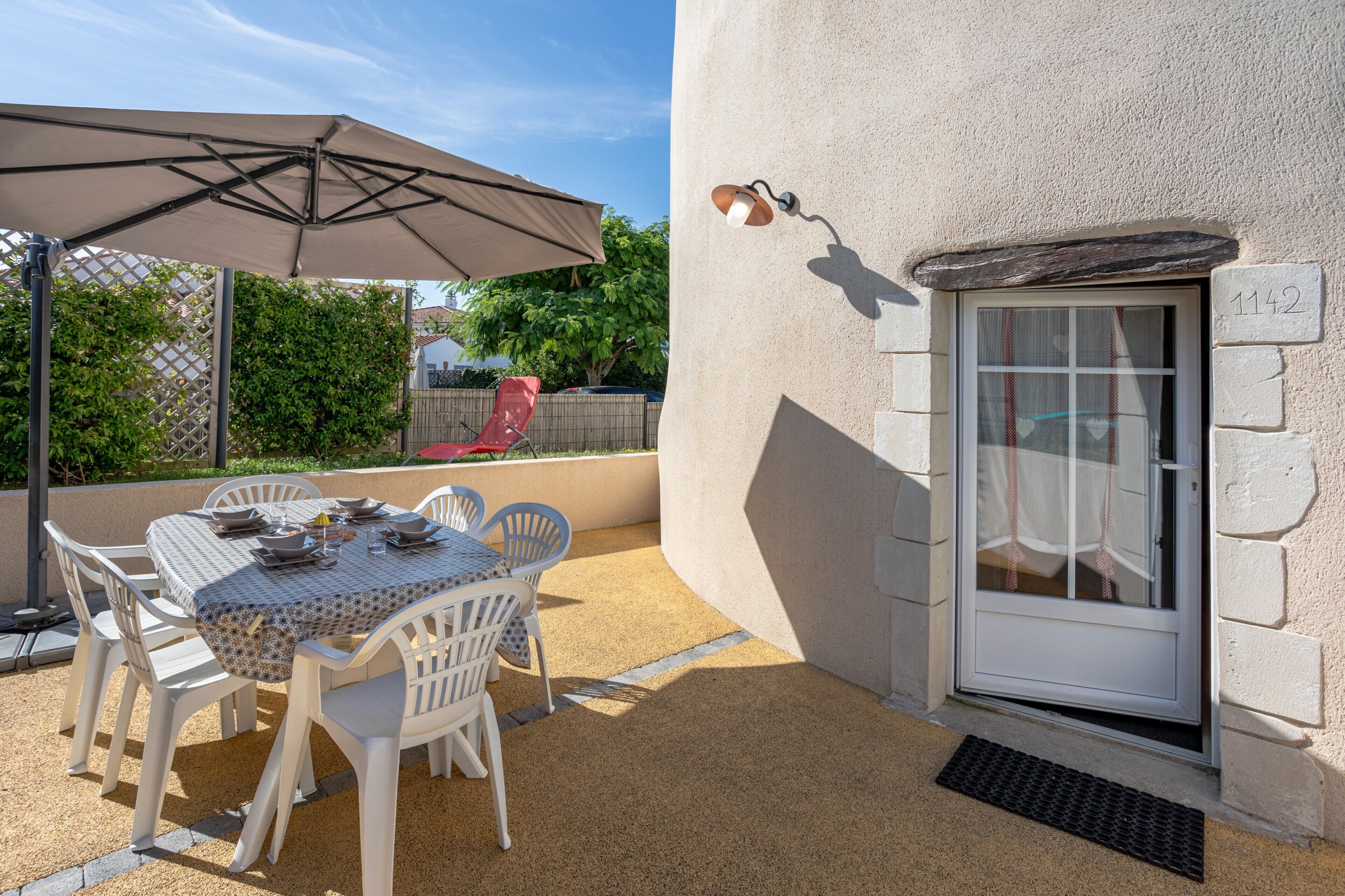 An outdoor patio with a table and chairs, a large umbrella, and a door with a number.