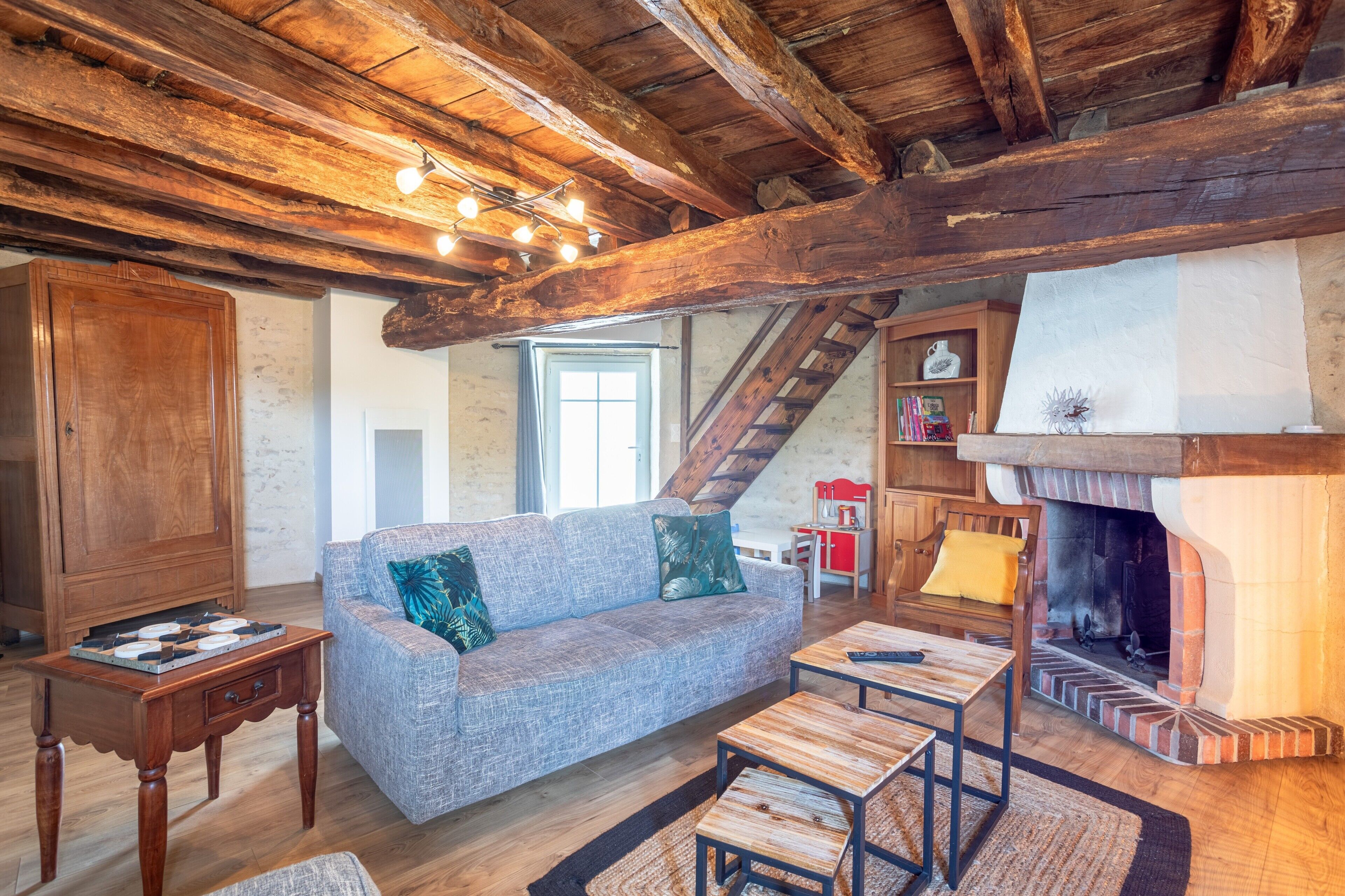 A rustic interior with exposed wooden beams, a fireplace, a sofa, and a wooden table.