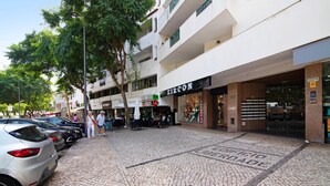 Una calle empedrada con coches estacionados, una tienda Zicon y mesas al aire libre.
