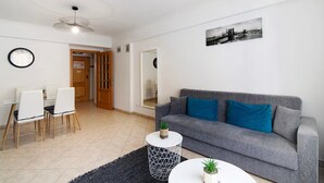 Un salón con un sofá gris, una mesa redonda y una mesa de comedor con sillas.