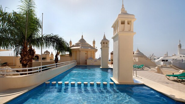 A swimming pool with a palm tree, lounge chairs, and a building with domes. - Studio Apartment "Puerto Marina Luxury" with Sea View & Wi-Fi (Benalmádena)