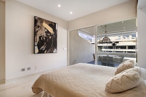 Une chambre d’hôtel moderne avec un grand lit, un tableau au mur et une vue sur la ville, visible à travers une porte vitrée.