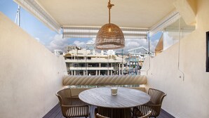 A balcony with a round table and chairs, a hanging light fixture, and a view of buildings in the background. - Studio Apartment "Puerto Marina Luxury" with Sea View & Wi-Fi (Benalmádena)