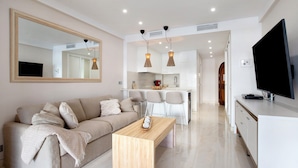 A modern living room with a sofa, a coffee table, and a TV. There is a kitchen area with a dining table and chairs. - Studio Apartment "Puerto Marina Luxury" with Sea View & Wi-Fi (Benalmádena)