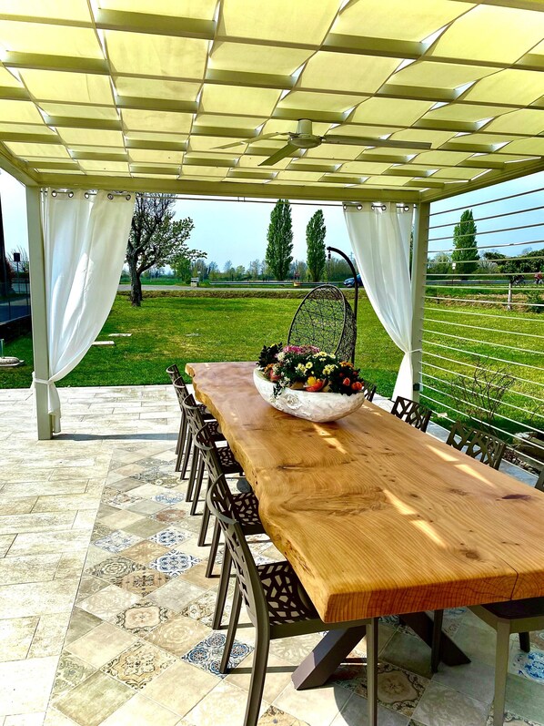 Un espace repas extérieur abrité, avec une longue table en bois, des chaises et un arrangement floral décoratif.