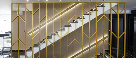 Un interior moderno con una escalera, un separador geométrico amarillo y un suelo de mármol pulido.