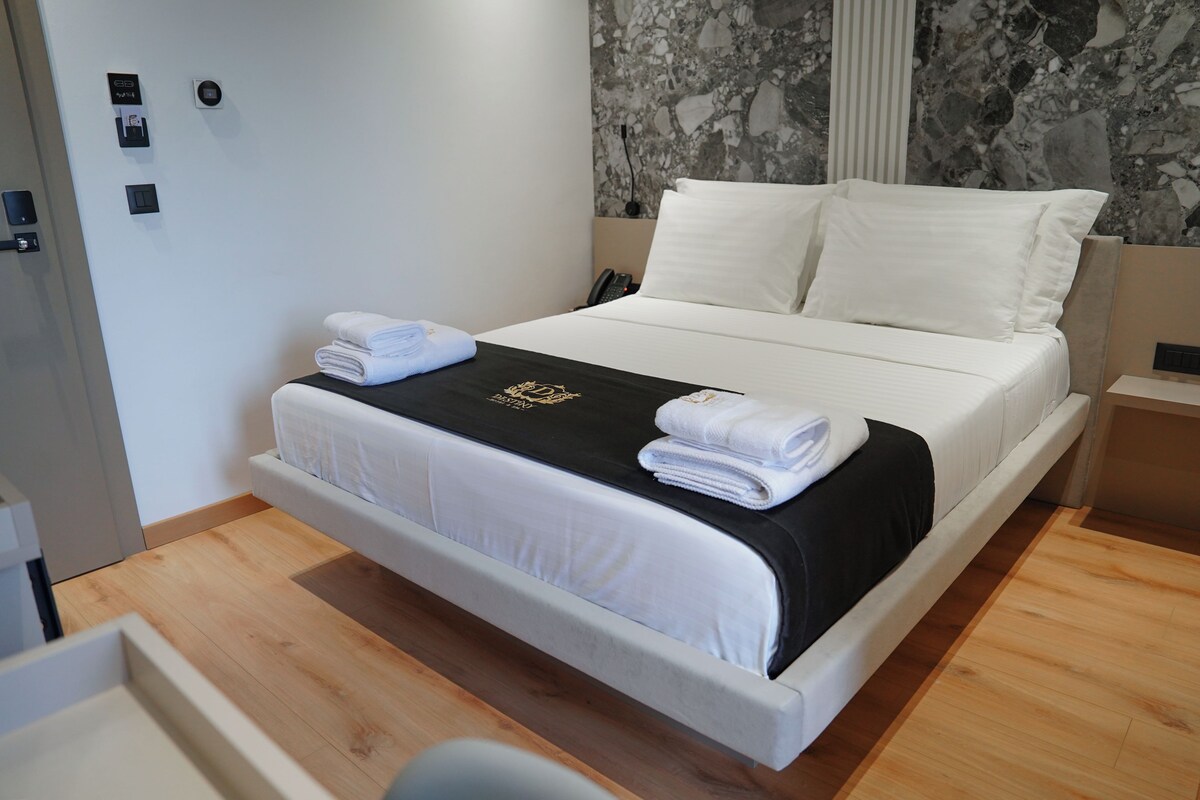A hotel room with a bed, a bedside table, a telephone, and a wall-mounted control panel.