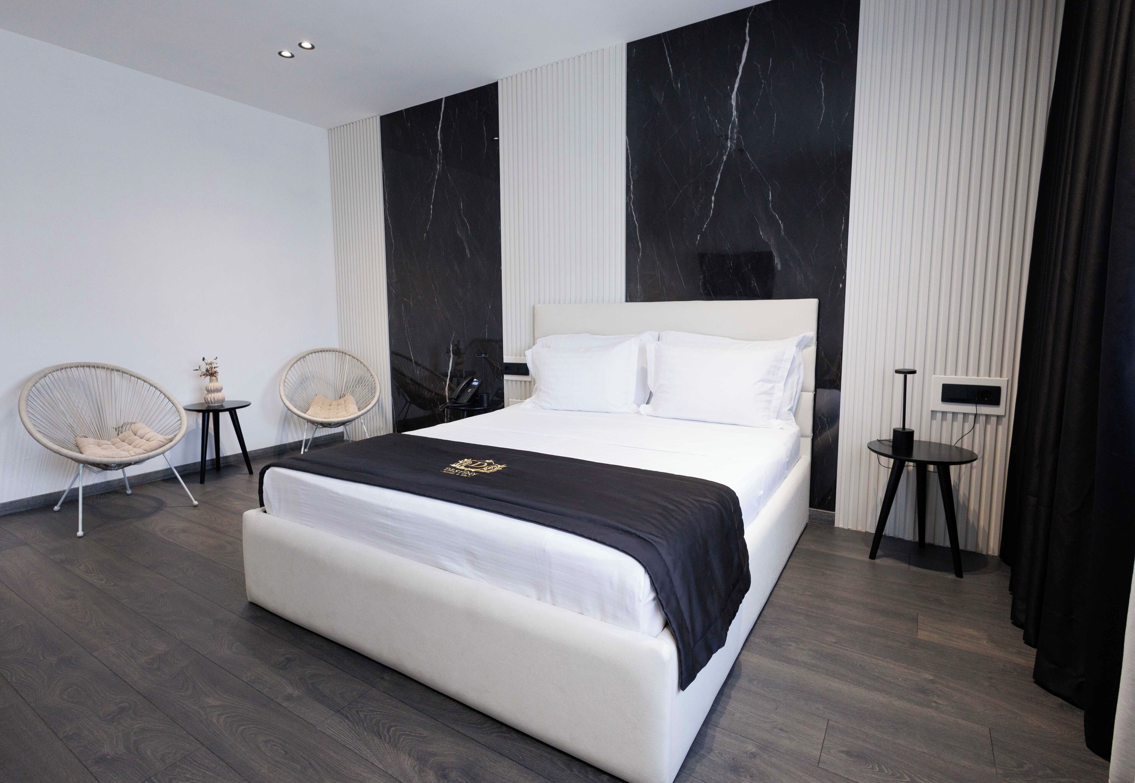 A modern bedroom with a large bed, two side tables, and two wicker chairs.