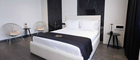 A modern bedroom with a large bed, two side tables, and two wicker chairs.