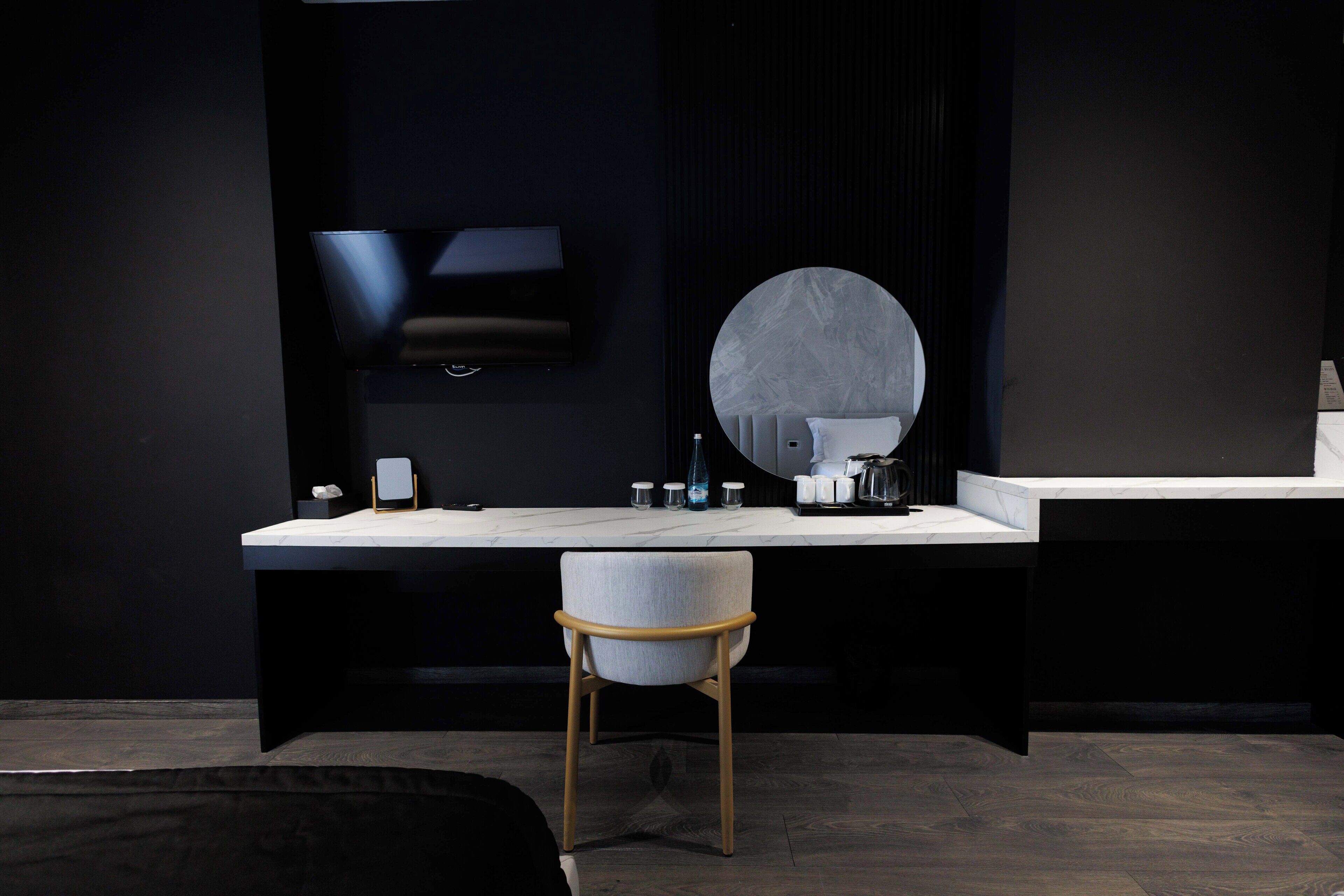 A modern bathroom with a dark theme, a round mirror, a white countertop, and a wooden chair.