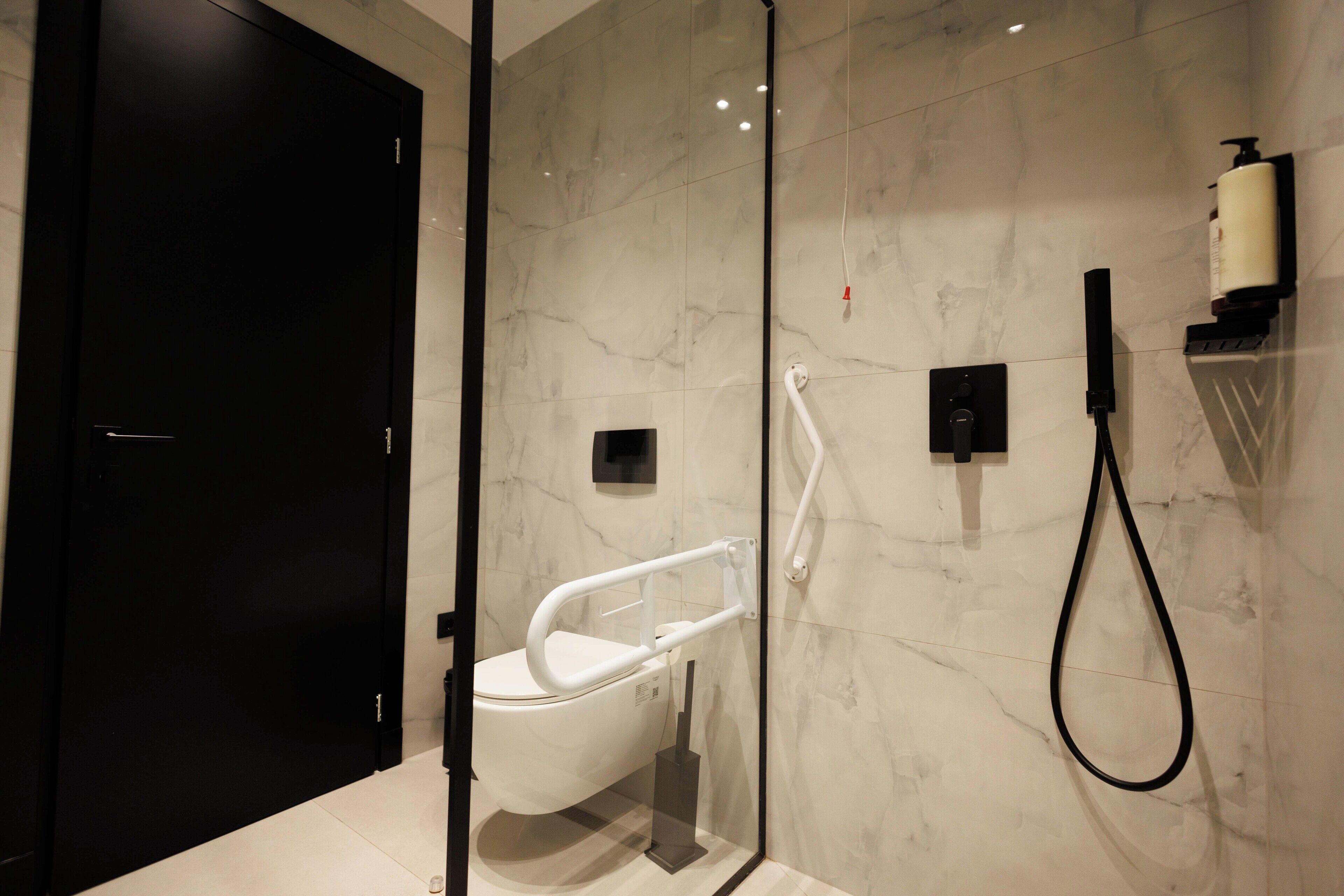 A modern bathroom with a glass shower enclosure, a white toilet, and a black door.