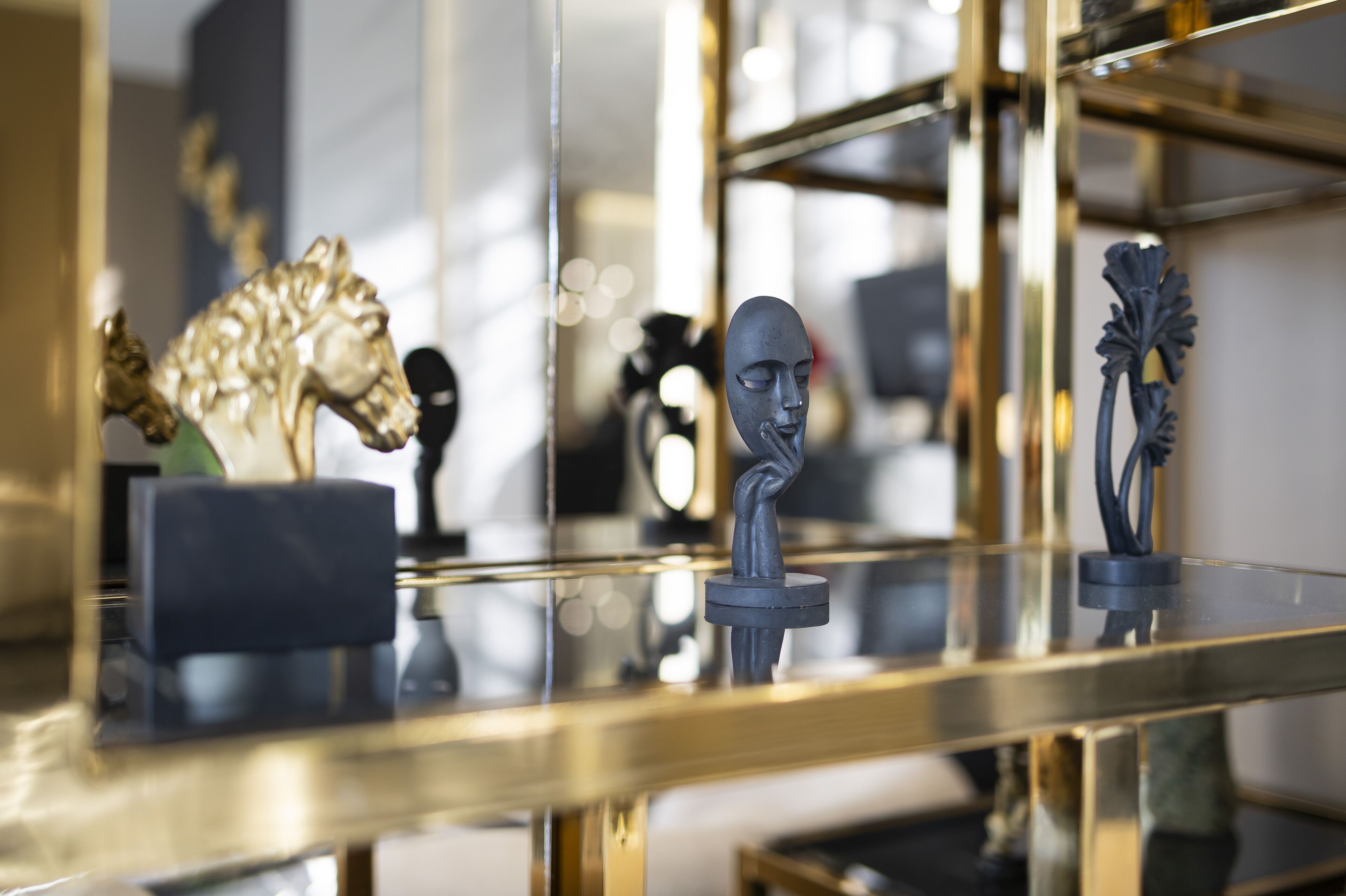 A room with a glass table displaying various sculptures and a gold-framed mirror.