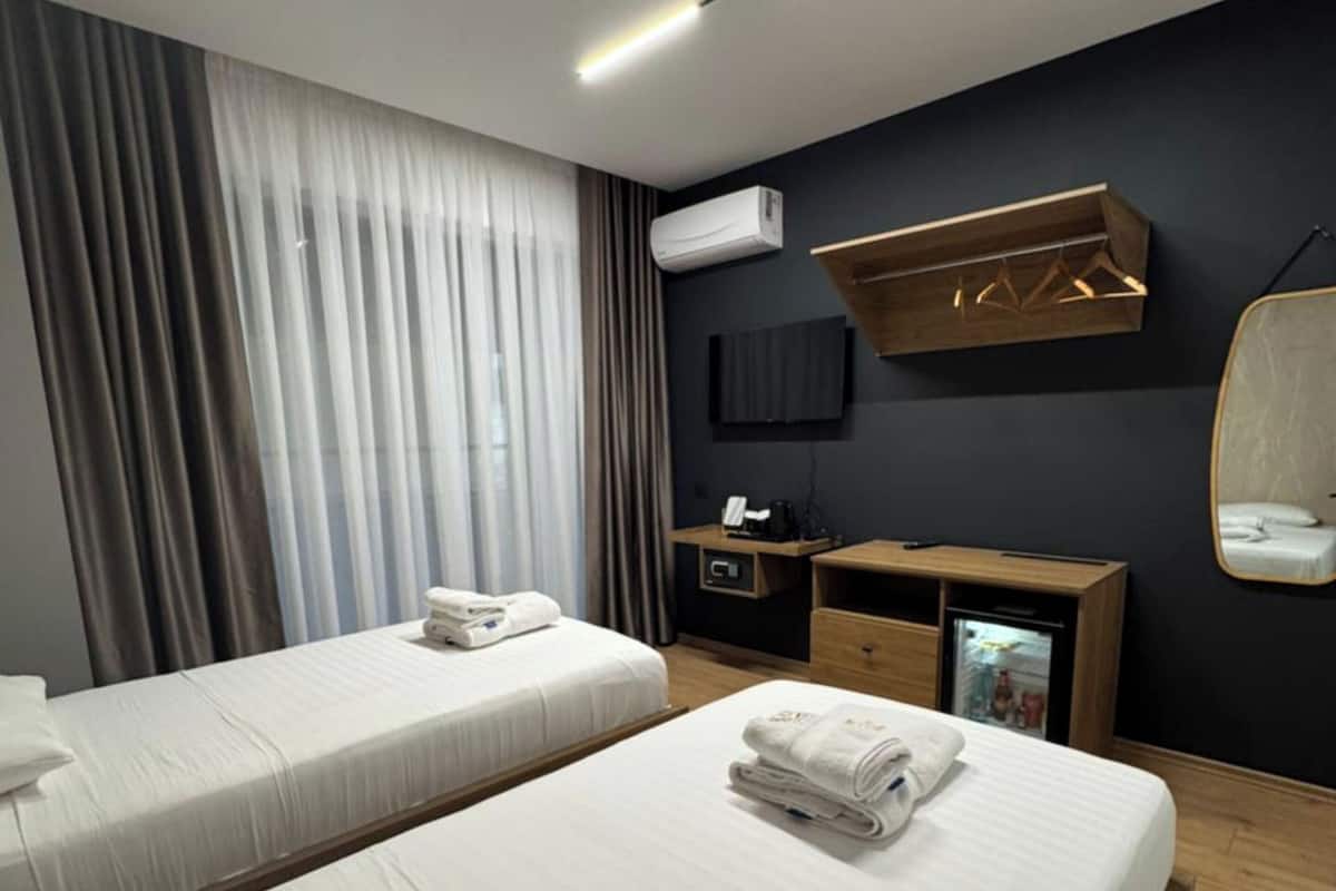 A hotel room with two beds, a TV, a minibar, and a wooden cabinet.