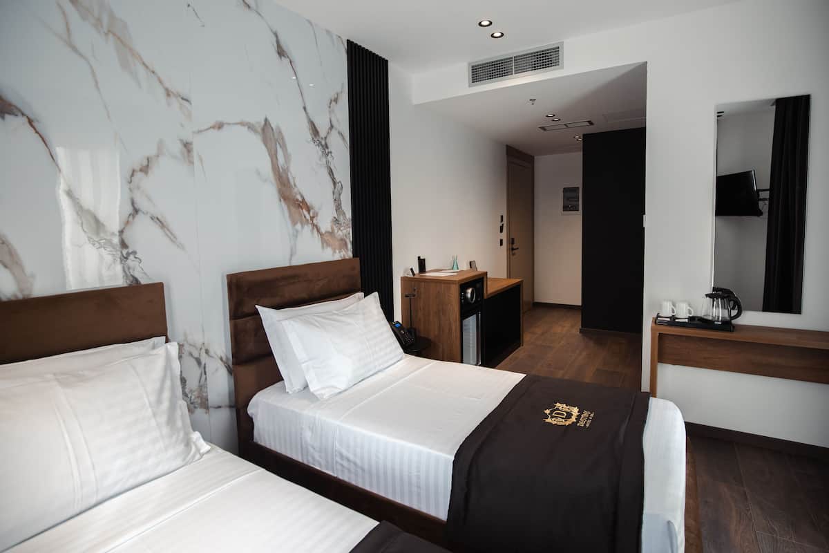 A hotel room with two beds, a wooden headboard, a marble wall, a desk with a mirror, and a television.