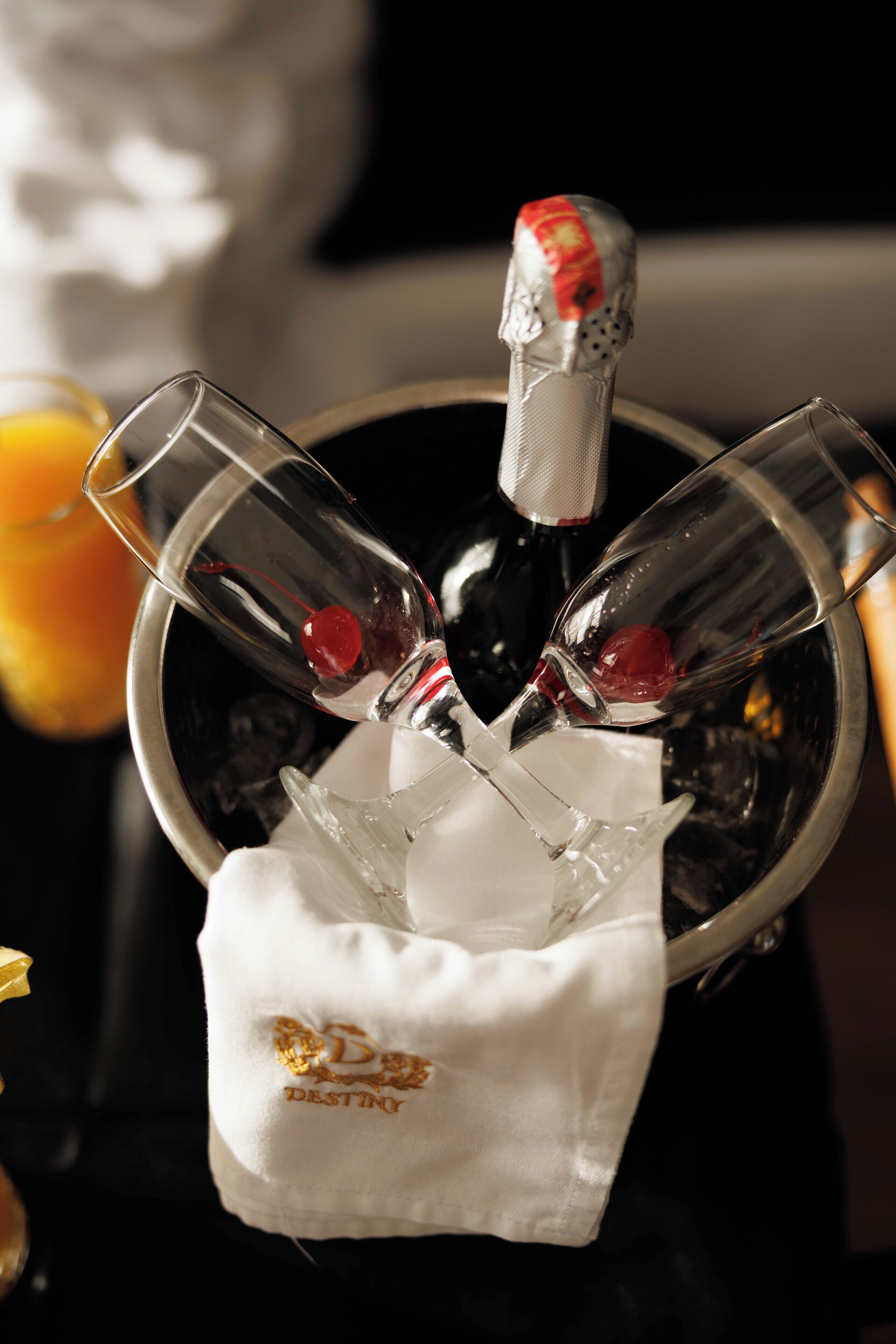 Un seau à champagne avec deux verres et une bouteille, une serviette blanche ornée d’un logo et un arrière-plan flou.