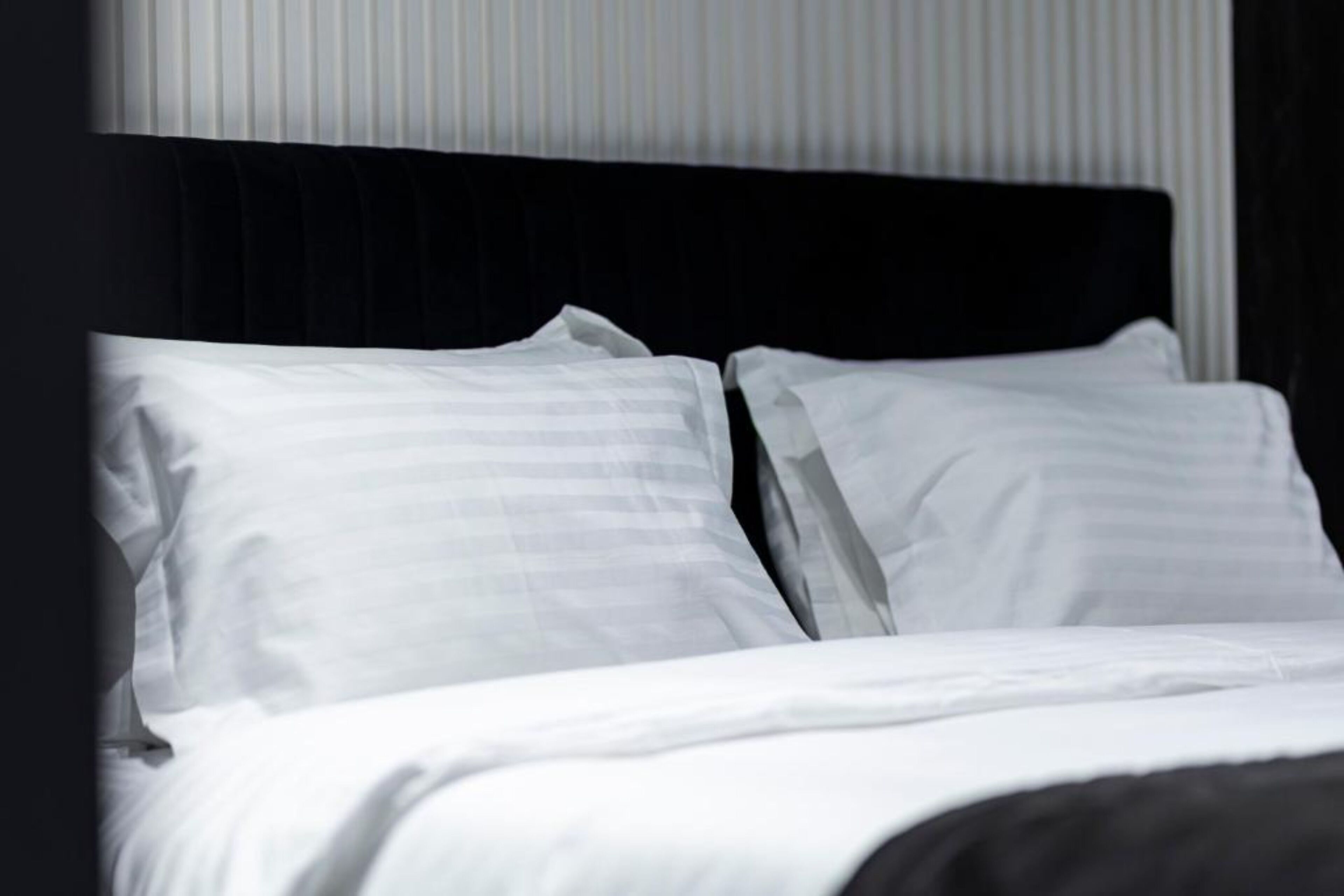 Una cama con ropa blanca y cabecera negra en una habitación de hotel.