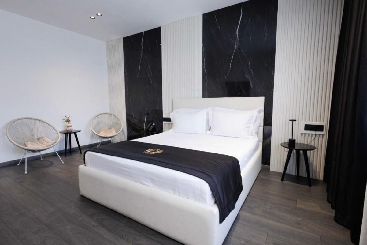 A modern bedroom with a large bed, two side tables, and two wicker chairs.