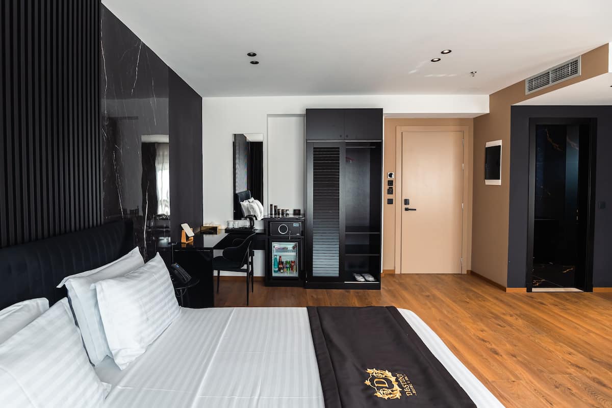 A modern hotel room with a large bed, a desk, a wardrobe, and a bathroom.