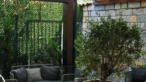 An outdoor patio area with wicker furniture, a large vase plant, and a stone wall. - Destiny Hotel (Kashar)