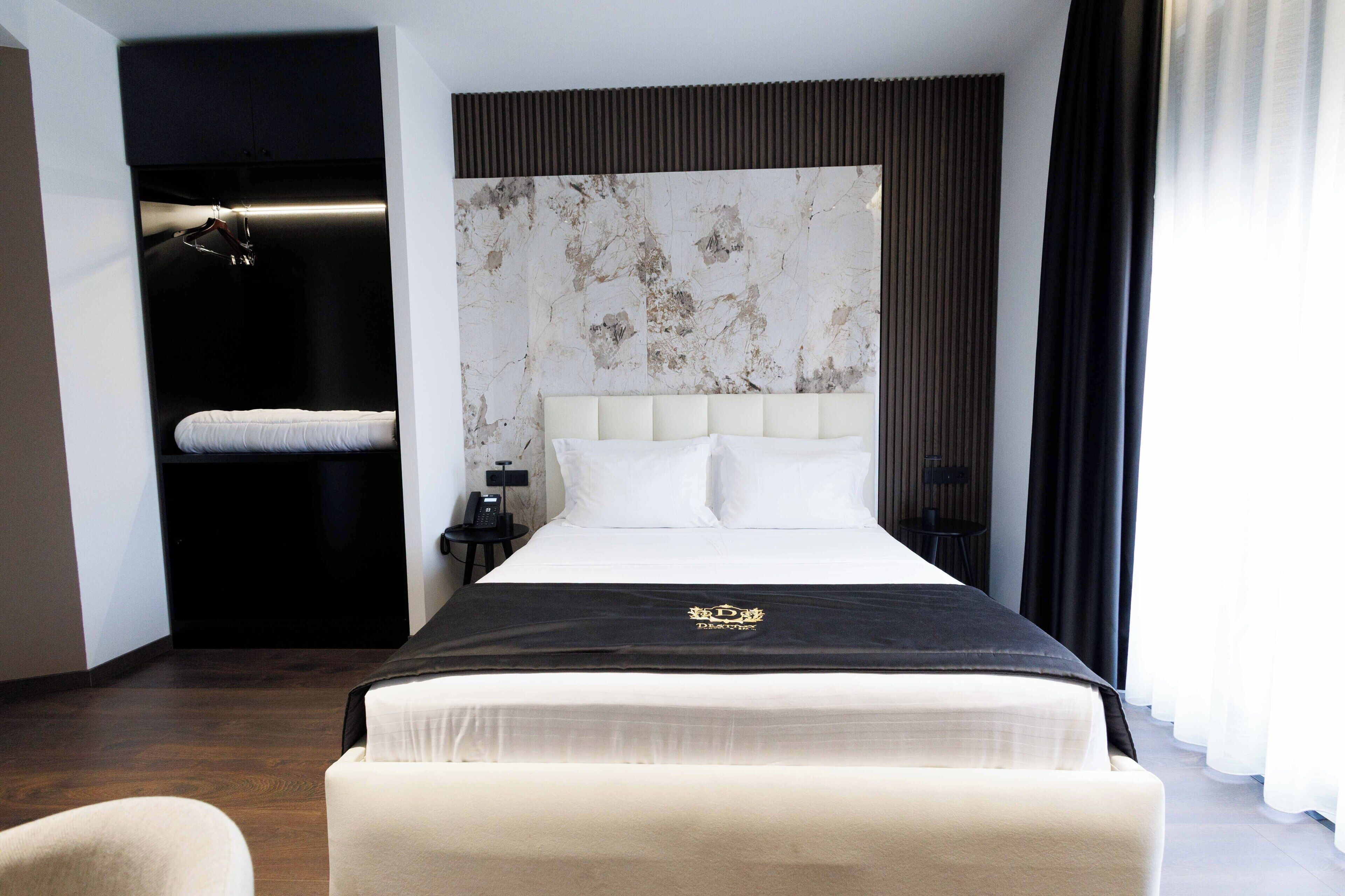 A hotel room with a large bed, a black headboard, and a marble-patterned wall.