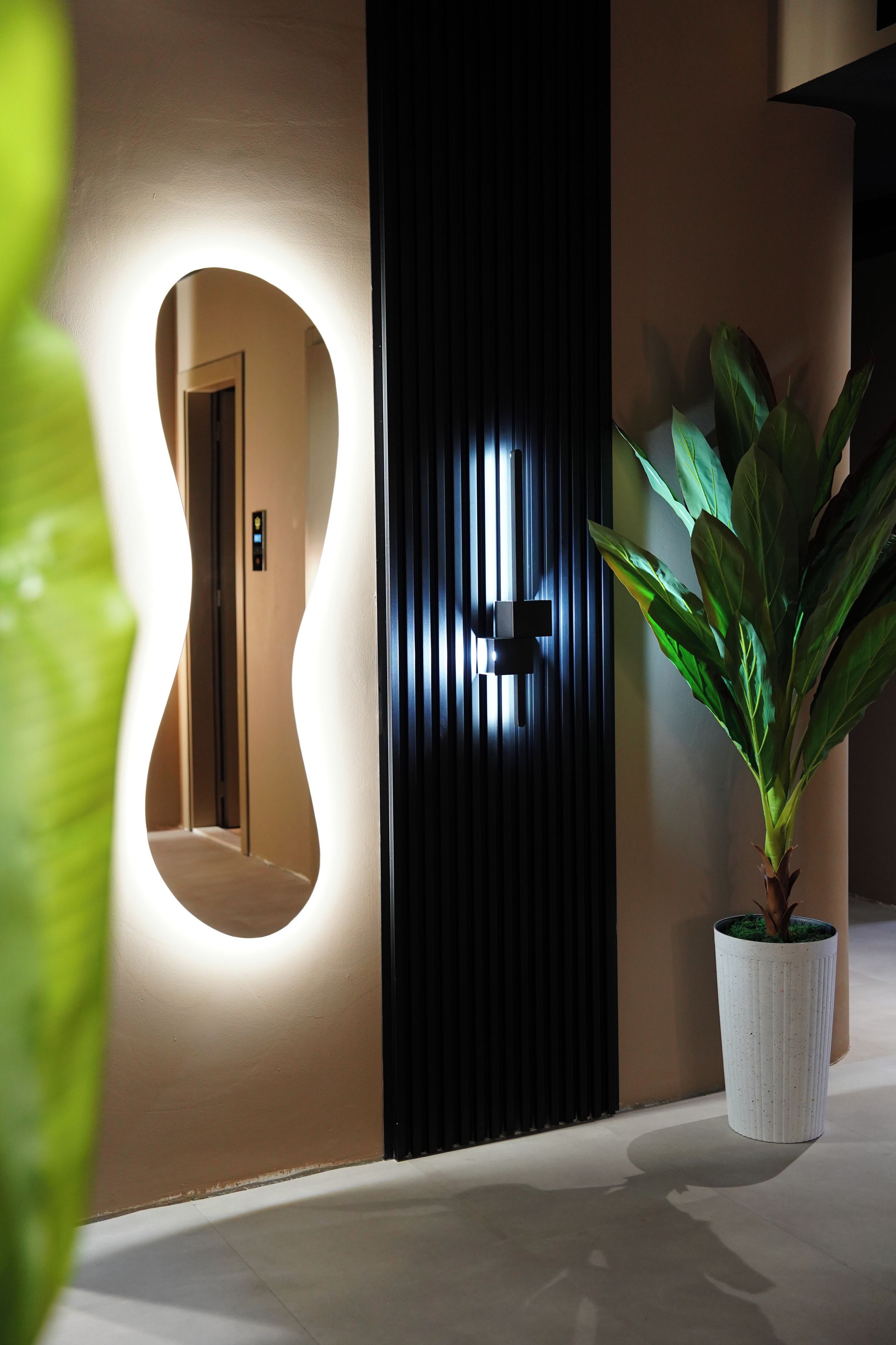 Un intérieur moderne agrémenté d’un luminaire mural original, d’une plante en pot et d’une porte au design à panneaux verticaux.