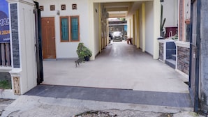 A corridor with a tiled floor, a potted plant, and a car parked at the end. - OYO Life 92637 Kost Arya Exclusive (Jambi)