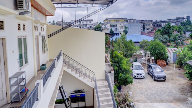 A residential area with a staircase leading to a balcony, a parked car, and a building with a metal roof structure. - OYO Life 92637 Kost Arya Exclusive (Jambi)