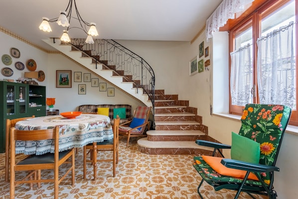 A staircase with a wrought iron railing, a dining area with a table and chairs, and a window with lace curtains.