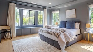 Un dormitorio con una cama grande, dos mesitas de noche, una ventana con cortinas y vistas al exterior.