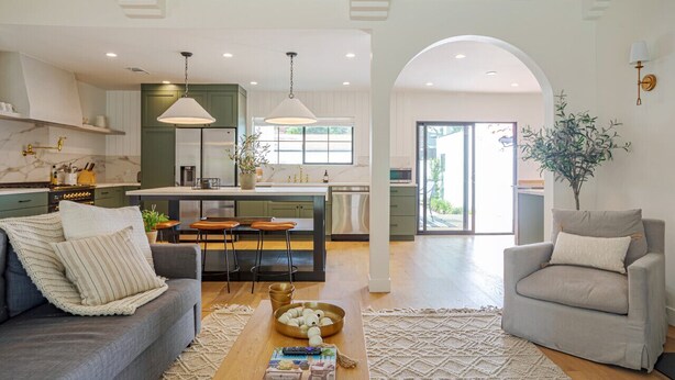 Cocina moderna con armarios verdes, una isla central, iluminación colgante y vistas al exterior.