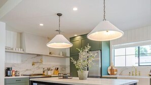 Una cocina moderna con una isla central, taburetes de bar, iluminación colgante y una planta en maceta.