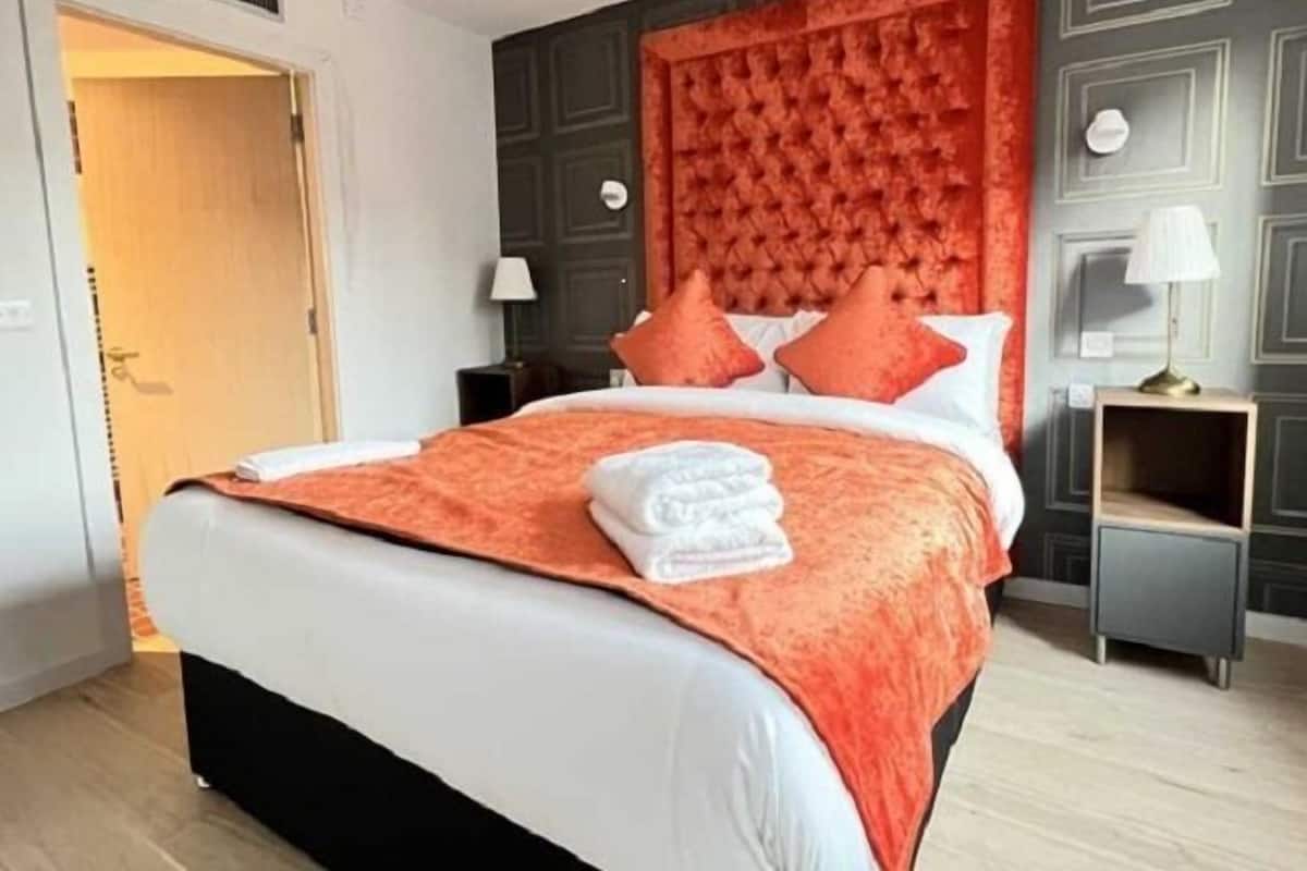 A hotel room with a large bed, a dark headboard, and a nightstand with a lamp.