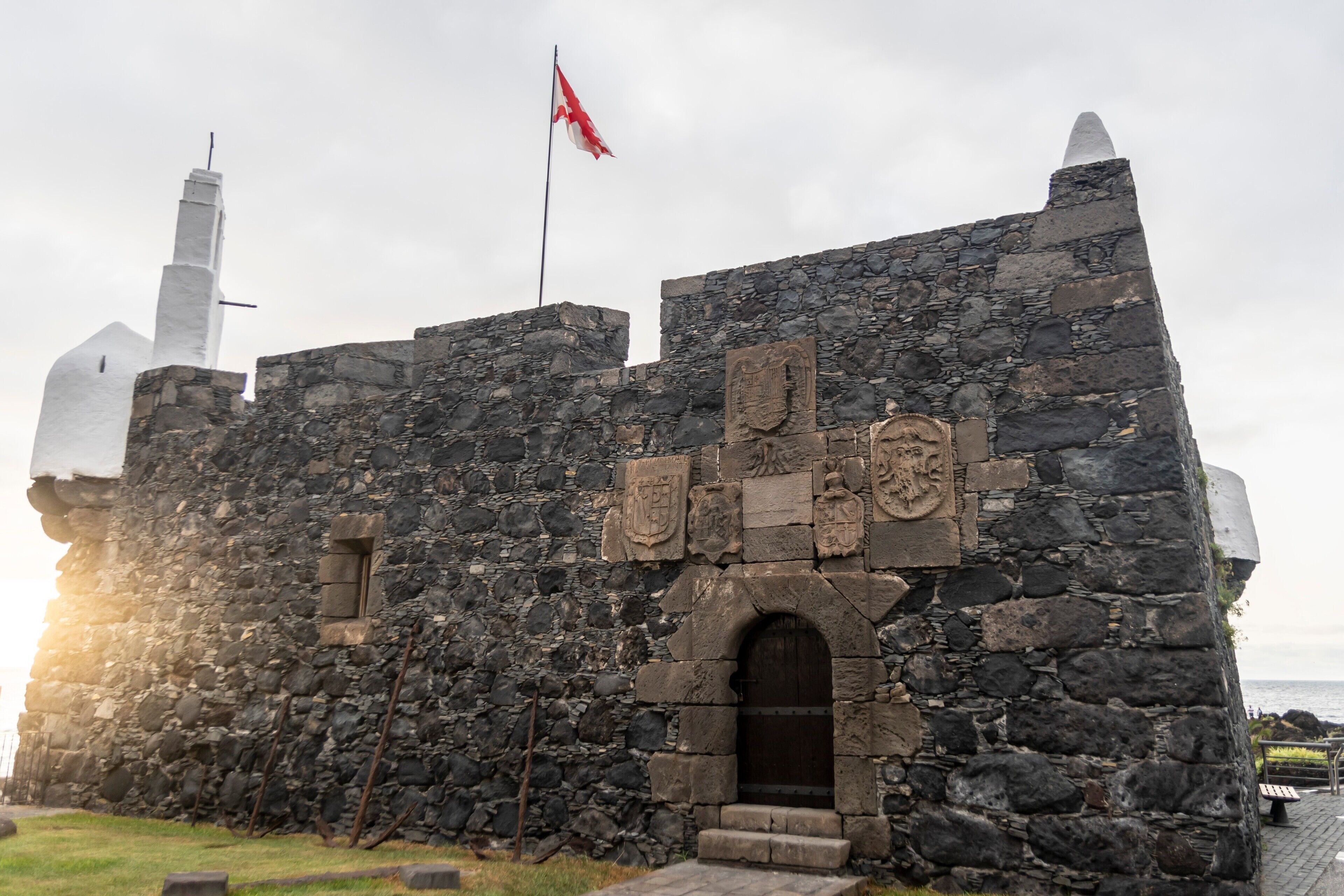 Un edificio de piedra con una bandera, un asta y un escudo de armas.