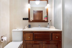 Een badkamer met toilet, wastafel, houten opbergmeubel en een spiegel met verlichting.