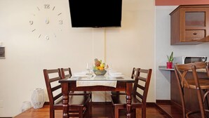 Un coin repas avec une table en bois, des chaises, une horloge et un téléviseur fixé au mur.