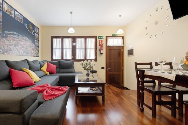 Een woonkamer met een bank, een salontafel, een eettafel gedekt voor twee personen en een wandklok.