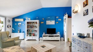 Una sala de estar con una pared azul de acento, una estantería blanca, un televisor de pantalla plana y un sofá estampado.